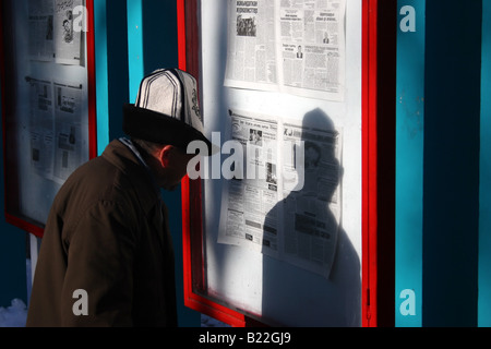 Ein Mann trägt einen traditionellen Hut liest eine öffentliche Zeitung angezeigt in einem Park in Bischkek, Kirgisistan Stockfoto