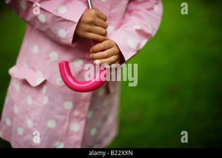 Fünf Jahre altes Mädchen im Garten mit Sonnenschirm an einem regnerischen Tag steht Stockfoto