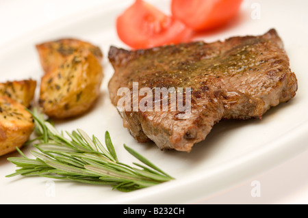 Nahaufnahme von gebratenem Rindfleisch und Kartoffeln mit Scheiben von Tomaten auf Teller Stockfoto