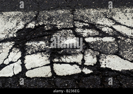 Nahaufnahme eines gerissenen weißen thermische Fahrbahnmarkierungen auf Asphalt Straße Stockfoto