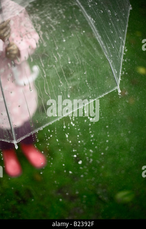 Fünf Jahre altes Mädchen im Garten mit Sonnenschirm an einem regnerischen Tag steht Stockfoto