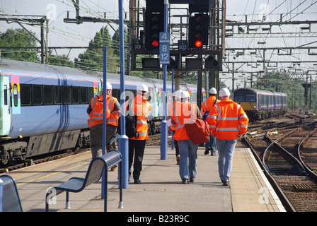 Rückansicht einer Gruppe von Wartungstechnikern verlässt den Bahnsteig von Shenfield und geht auf den belebten Bahngleisen Essex England UK in Richtung der Züge Stockfoto