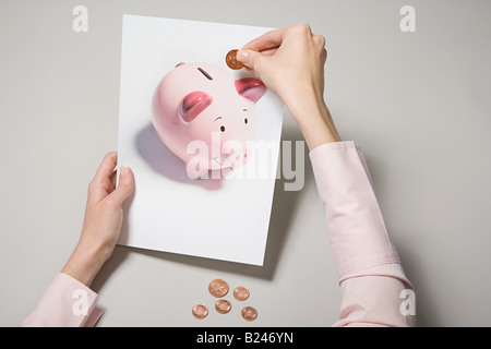 Eine Frau hält ein Foto von einem Sparschwein und eine Münze Stockfoto
