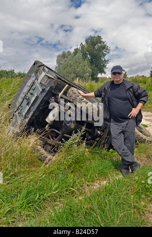 Fahrer, die seinem Land Rover Serie 2a Leichtgewicht auf seiner Seite stolz präsentieren, nachdem es von der Strecke in einen Graben rutschte. Stockfoto