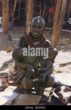 Junge Samburu Frau hockt vor ihrer Hütte hält ihre Zwillingsschwester Babys nördlichen Kenia in Ostafrika Stockfoto