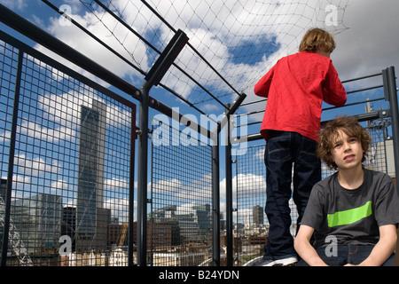 Zwei Jungs hinter dem schützenden Zaun auf einem Dach in East London Ocerlooking der City von London der Broadgate Tower entworfen von ar Stockfoto