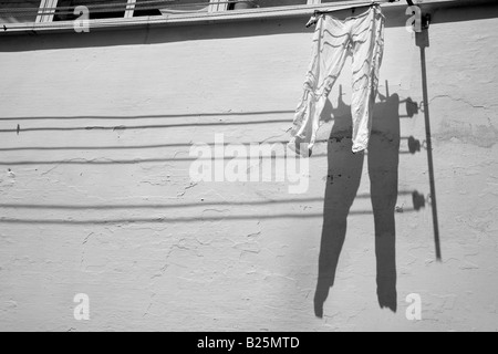 Weiße Hosen beim Trocknen Linie gegen weiß gestrichenen Wand mit Schatten in der Stadt in Apulien Italien Stockfoto
