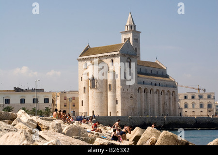 Die Kathedrale - gewidmet St. Nikolaus den Pilger - in Trani, Italien. Menschen zum Sonnenbaden und Schwimmen im Vordergrund. Stockfoto