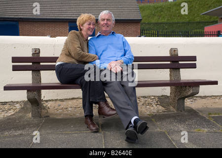Ein pensionierter Mann und eine Frau sitzen zusammen auf einer Bank in der Nähe von Roker Strand in England. Stockfoto