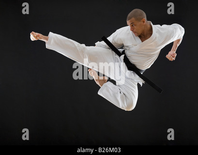 Hispanische männlichen Karate Schwarzgurt treten in Luft Stockfoto