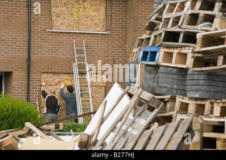 Zwei Männer an Bord, Fenster eines Hauses neben einem großen Lagerfeuer um Brandschäden zu verhindern.  Neue Mossley, Newtownabbey Stockfoto