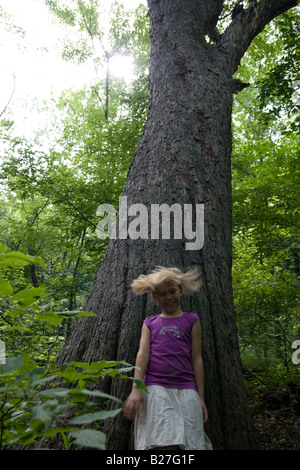 Ein junges Mädchen Spinnen vor einem großen Baum in einem Wald. Stockfoto