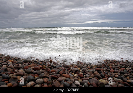 Kiesstrand mit Kies und Steinen, stürmische Wellen und grauen Himmel Stockfoto