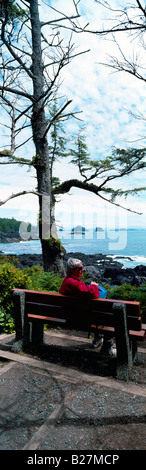 West Küste von Vancouver Island, BC, Britisch-Kolumbien Kanada - Wanderer sitzen auf einer Parkbank entlang der zerklüfteten Küste in der Nähe von Ucluelet Stockfoto