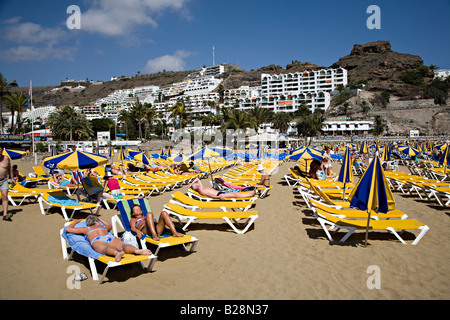 Menschen am Strand liegen mit Resort Ferienwohnungen auf Hügel Puerto Rico Gran Canaria Spanien Stockfoto