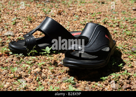 Schwarz offen toe Sandalen aus Leder hergestellt in Indien gehalten, um trocken unter der Sonne auf rauem Untergrund Steinchen Kies und Gras neue Stockfoto