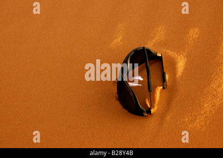 Sonnenbrille im Sand sind von der untergehenden Sonne beleuchtet, während der Wind Sand Mauern um sich herum aufbaut Stockfoto