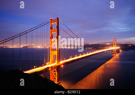 Golden Gate Bridge glüht vor Hintergrund beleuchtete Skyline der Bay Bridge und San Francisco Stockfoto