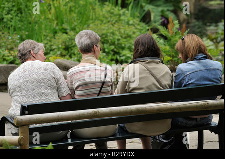 Menschen im Park: Sitzen auf einer Bank zwei junge Studenten Chat mit zwei Senioren. Stockfoto