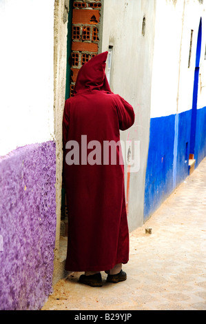 Mann mit traditionellen, dunklen Rot marokkanischen dejellaba mit der Haube stehen in einer offenen Tür. Stockfoto