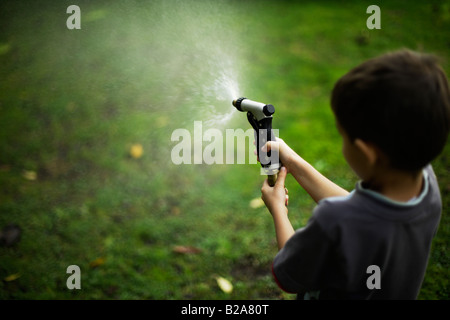 Sechs Jahre alten Baue Sprays Rasen mit Schlauch und Messing Spritzpistole Mischlinge indischen ethnischen und kaukasischen Stockfoto