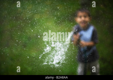 Gartenschlauch besprüht ein Glas Fenster sechs Jahre alter Junge Mixed race indischen ethnischen kaukasischen Stockfoto