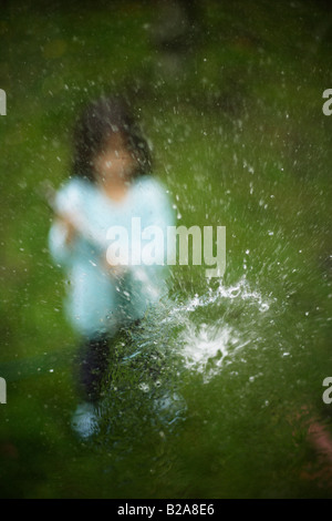 Gartenschlauch besprüht ein Glas Fenster fünf Jahre altes Mädchen Mixed race indischen ethnischen kaukasischen Stockfoto