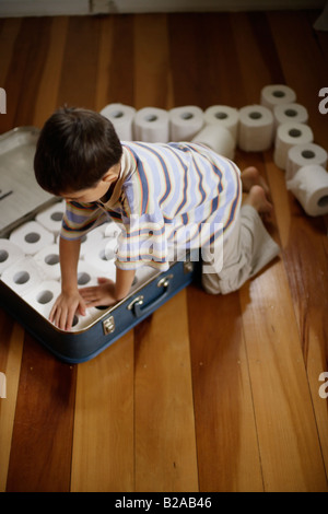 Sechs Jahre alter Junge packt Toilettenpapierrollen in Koffer Mischlinge indischen ethnischen und kaukasischen Stockfoto