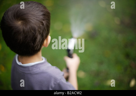 Sechs Jahre alten Baue Sprays Rasen mit Schlauch und Messing Spritzpistole Mischlinge indischen ethnischen und kaukasischen Stockfoto