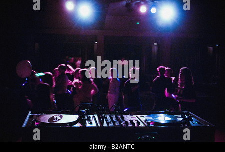 Überfüllte Tanzfläche in einem Nachtclub, von hinten gesehen von einem DJ-Mixer und Plattenspieler. Stockfoto