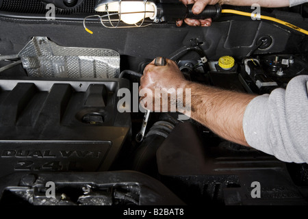 Kfz-Mechaniker mit Schraubenschlüssel und Arbeit Licht arbeitet am Motor Stockfoto