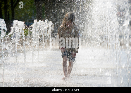 Kleine, 5 jährige Mädchen zu Fuß durch Wasserstrahlen in einem Brunnen Stockfoto