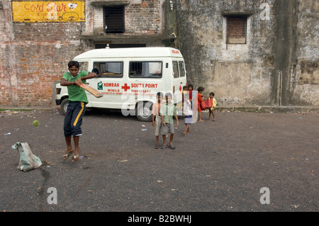 Wie Cricket der indischen Nationalsport ist, spielen Kinder und Jugendliche es überall, in diesem Fall vor einen Krankenwagen belon Stockfoto