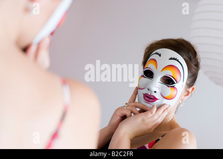 junge Frau hinter der Maske Spiegel betrachten Stockfoto