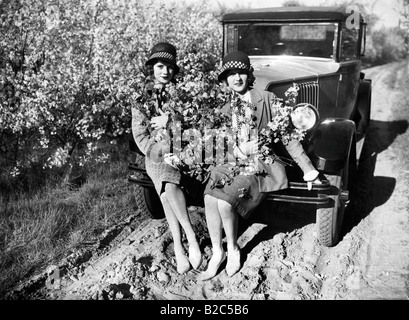 Zwei Frauen mit Blüten sitzen auf einem Auto, historisches Foto, ca. 1920 Stockfoto