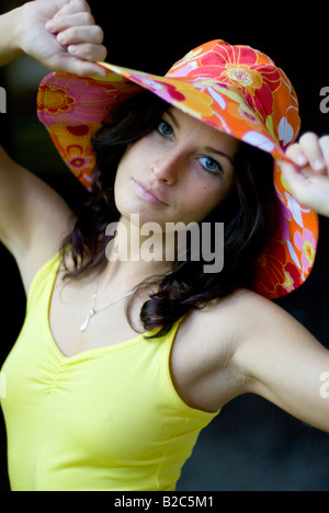 niedliche dunkelhaarige Frau im gelben Hemd mit einem bunten Hut Stockfoto