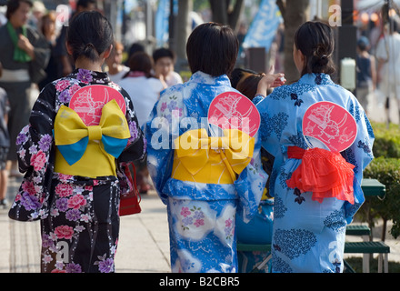 Drei Mädchen in bunte Baumwolle Yukata-Roben gekleidet mit Obi Gürtel hält, dass Fans Spaziergang in der lokalen kleinen Stadtfest Stockfoto