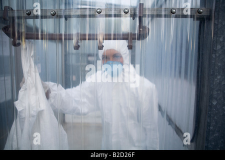 Arbeiter in Schutzmaske und Anzug hinter Kunststoff Wand Stockfoto