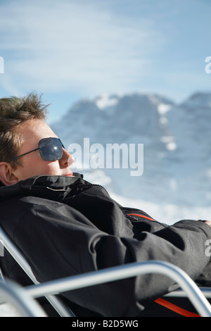 Mann in Mantel und Sonnenbrille sitzt im Sessel von Bergen Stockfoto