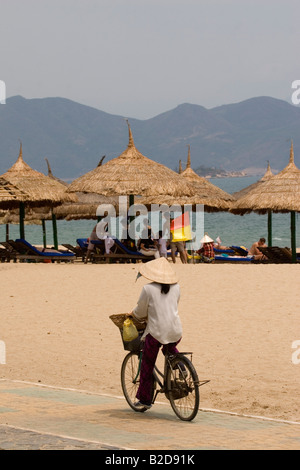 Eine Vietnamesin Zyklen Strand von Nha Trang. Sie verdunkelt sich gut vor der Sonne. In der Zwischenzeit Sonnenbaden Touristen am Strand. Stockfoto