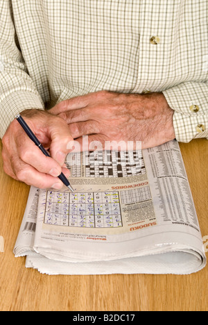 Vertikale Porträt ein älterer Herr tut das Sudoku-Rätsel in seiner Tageszeitung Stockfoto