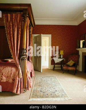 Roten Damast Vorhänge auf antiken Schlafzimmereinrichtungen Bett im roten Schlafzimmer mit kleiner Teppich auf Teppich Creme Stockfoto