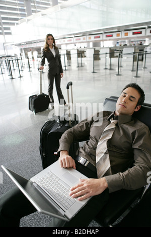 Müde Geschäftsmann mit Laptop im Flughafen mit Geschäftsfrau hinter. Stockfoto