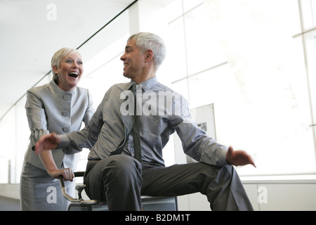 Reife Frau treibt Mann auf Gepäckwagen am Flughafen. Stockfoto