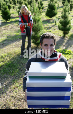 Junger Mann hält Weihnachtsgeschenke im Freien mit verärgert Frau hinter. Stockfoto