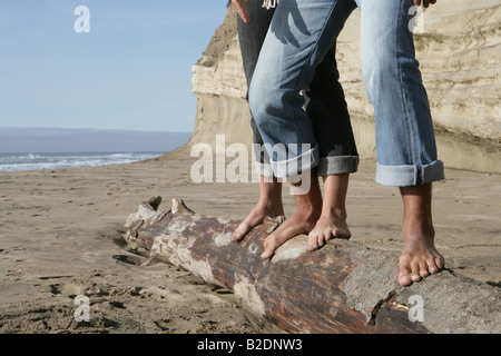 Blick auf paar balancing auf Baumstamm am Strand beschnitten. Stockfoto