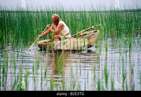 Neolithische Reenactment. Steinzeitmensch mit Fisch Speer paddeln Tier verstecken Coracle Boot auf Reed Ufer See. Kilmartin, Schottland Stockfoto