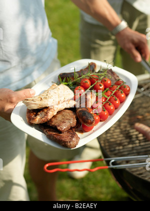 Nahaufnahme von jemandes Hand mit Wurst und Cherry-Tomaten auf Teller Stockfoto