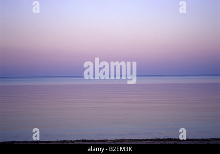 Rosa & lila Sonnenuntergang über dem Meer spiegelt sich in Wasser vom Horizont zum Strand. Ein Foto von Pink-, violett- & Mauves Wellen & Himmel Stockfoto