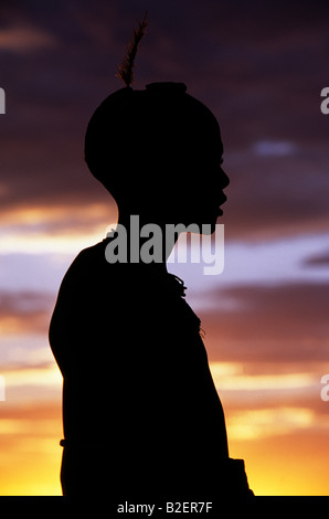 Eine Dassanech Mädchen lehnte sich gegen einen Ballen von Viehfutter auf einer erhöhten Plattform ist gegen den Abendhimmel abhebt. Stockfoto